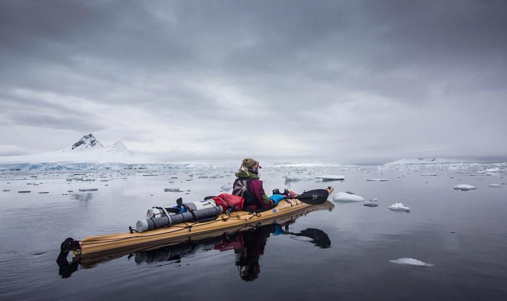 A kayaker in a sea kayak among drifting ice floes under an overcast sky