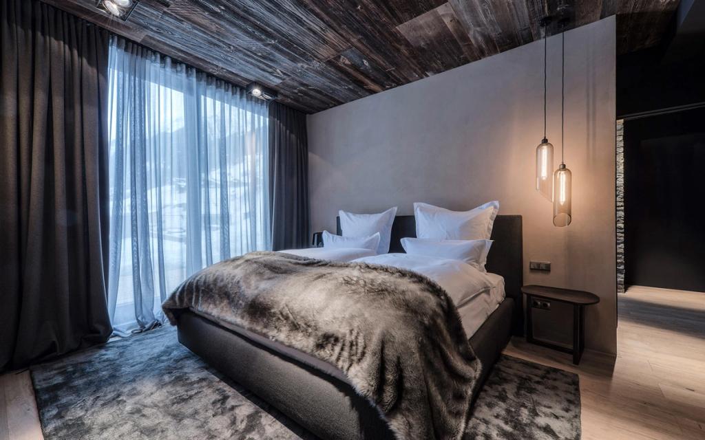 A room with a wooden ceiling, a fur throw on the bed and a panoramic window