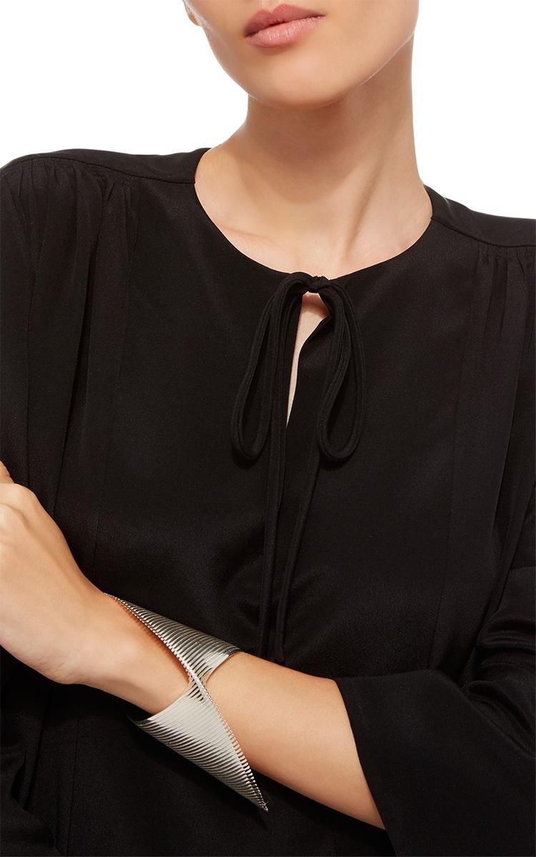 A silver ribbed bracelet on the wrist of a model in a black dress