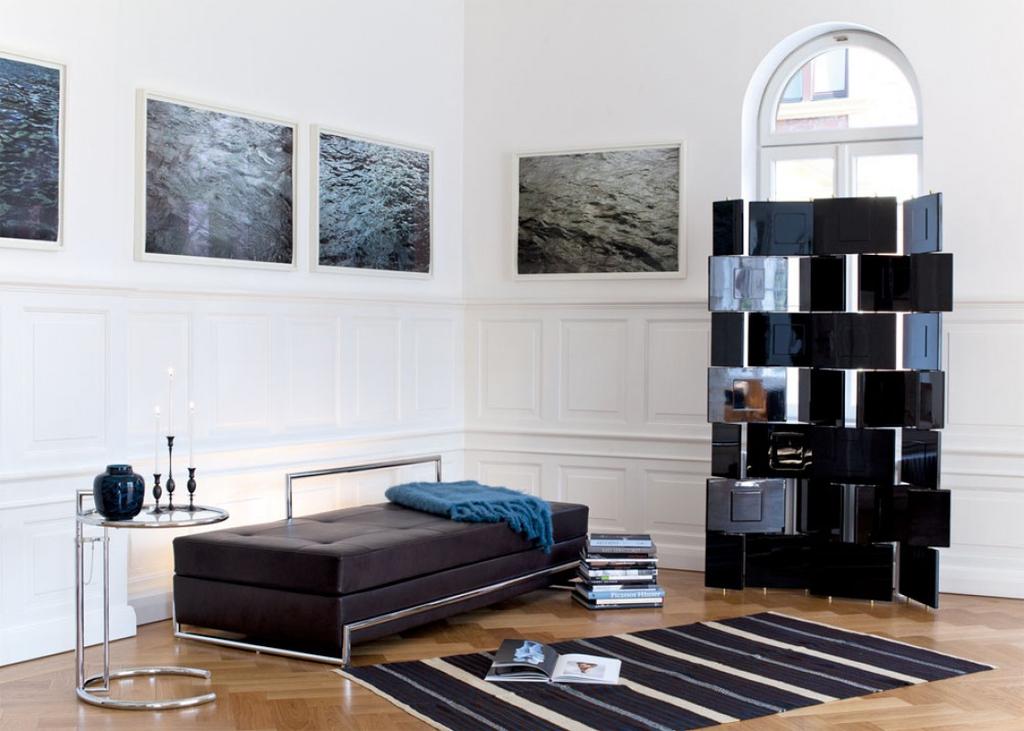 A bright living room with panoramic glazing: a black daybed, light furniture and a dog on the floor