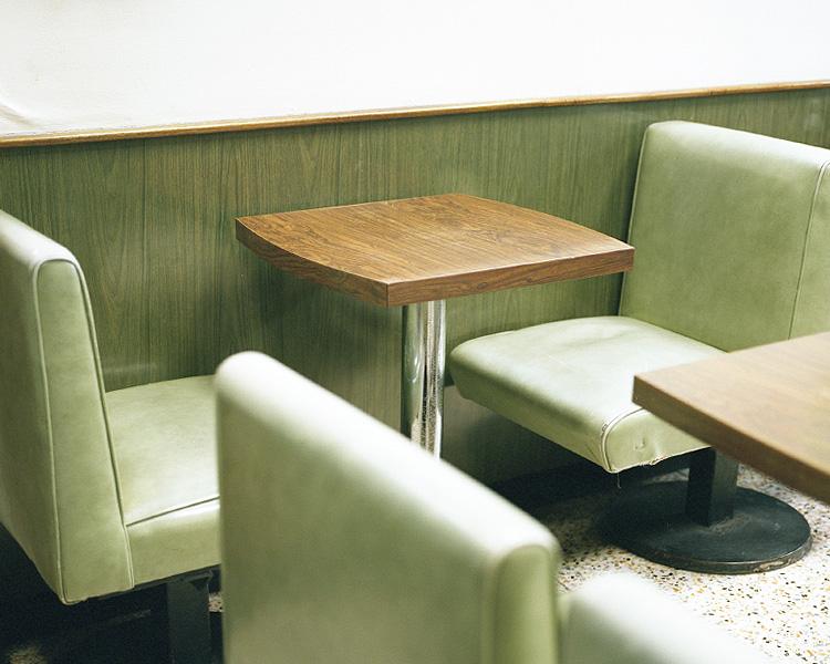 Light green vinyl sofas and a small wooden table in the corner of a café with a terrazzo floor