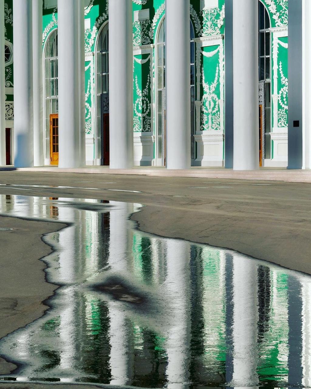 The white-and-green colonnade of the Hermitage reflected in a puddle on the square
