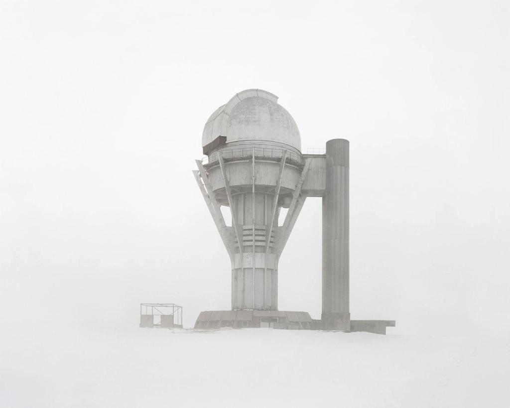 A concrete observatory tower with a telescope dome shrouded in dense snowy fog