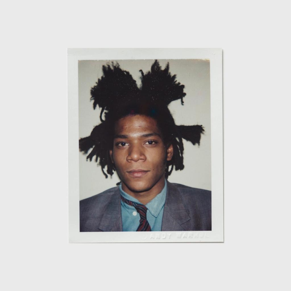 A Polaroid portrait of Jean-Michel Basquiat with his hair in wild dreadlocks, wearing a jacket and tie