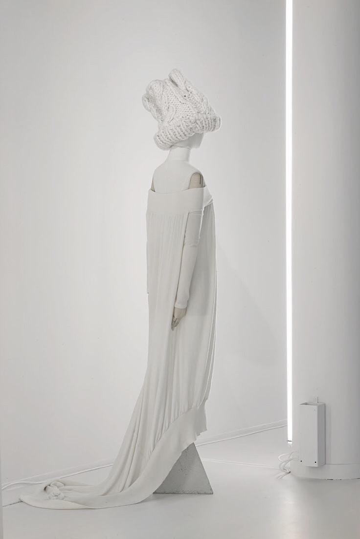 A mannequin in a white pleated dress with a long train and a knitted headpiece