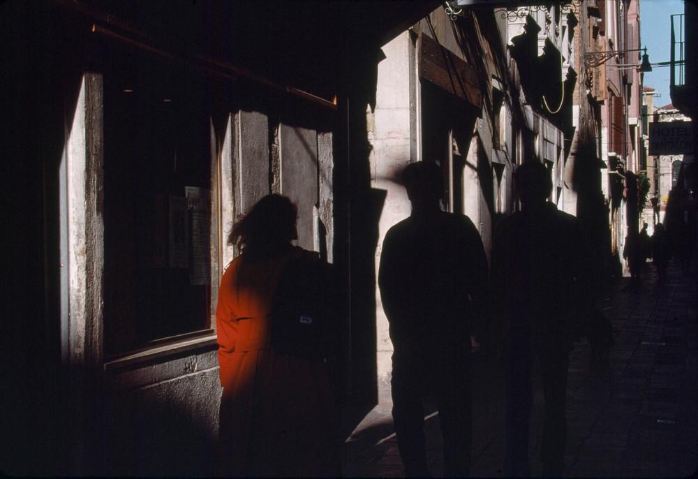 A narrow Venetian alley, a woman in orange at a shop window, silhouettes of passers-by