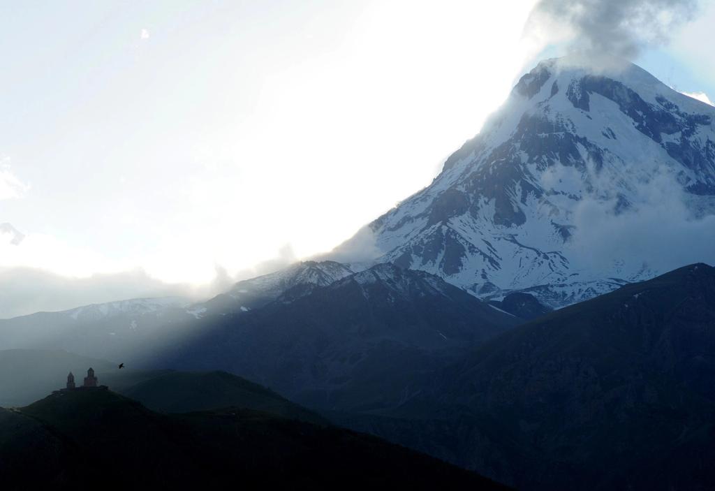 The snow-covered summit of Mount Kazbek shrouded in clouds, with the silhouette of Gergeti Trinity Church below