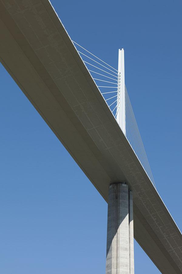 A cable-stay pylon of the Millau Viaduct and the deck above green hills, viewed from below
