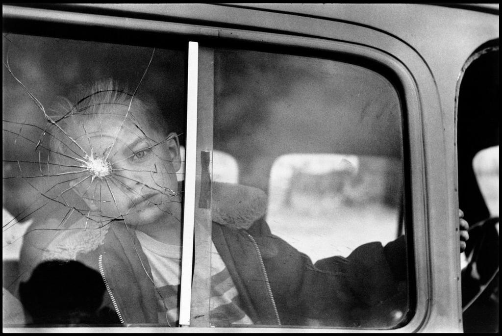 A boy looking through a cracked and shattered car window