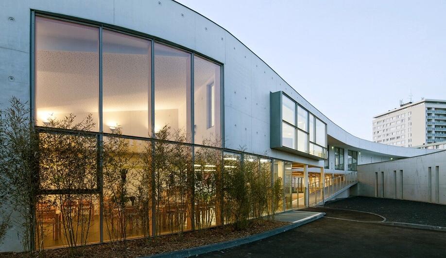 The curved concrete façade of Ecole Jean-Moulin school with large stained-glass windows