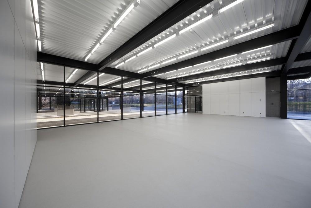 The open interior of a glass pavilion with steel beams and a ribbed ceiling