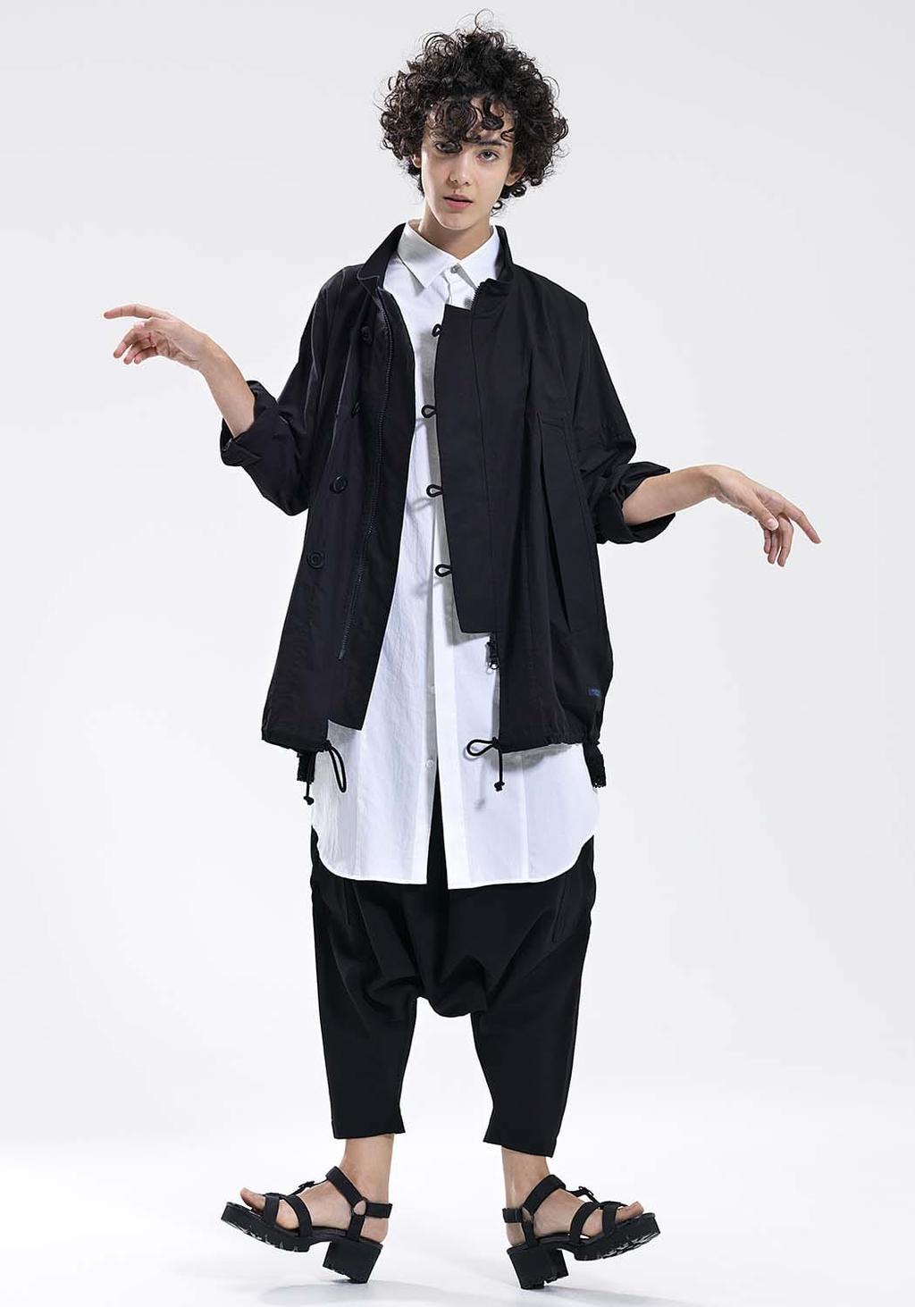A model in a black parka jacket, white shirt, and wide black trousers