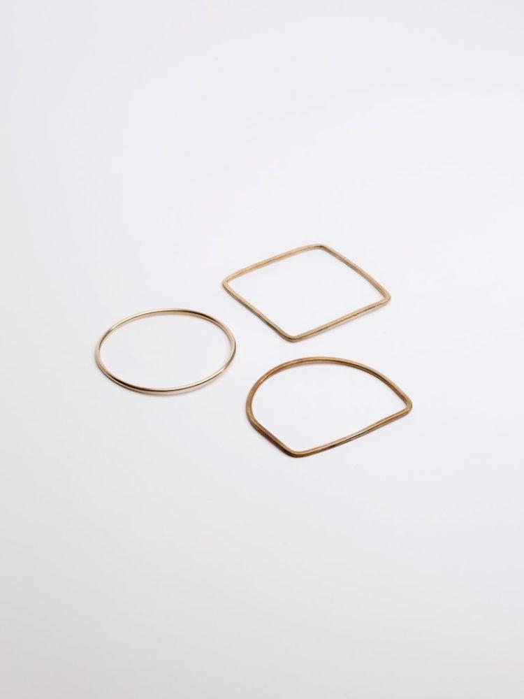 Three delicate gold rings of different geometric shapes against a light background