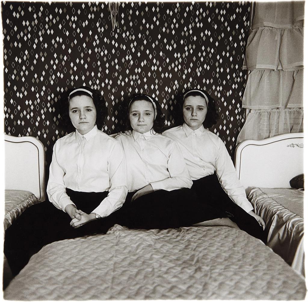 Three teenage girls in white blouses sitting on a bed against a wall with a diamond-pattern wallpaper