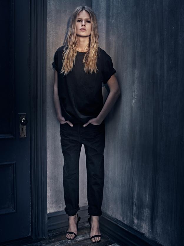Model in an all-black look with a T-shirt and trousers against a concrete wall