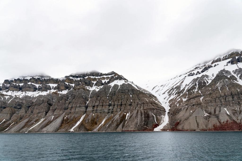 The layered mountain slopes of Svalbard with patches of snow above the dark waters of the fjord