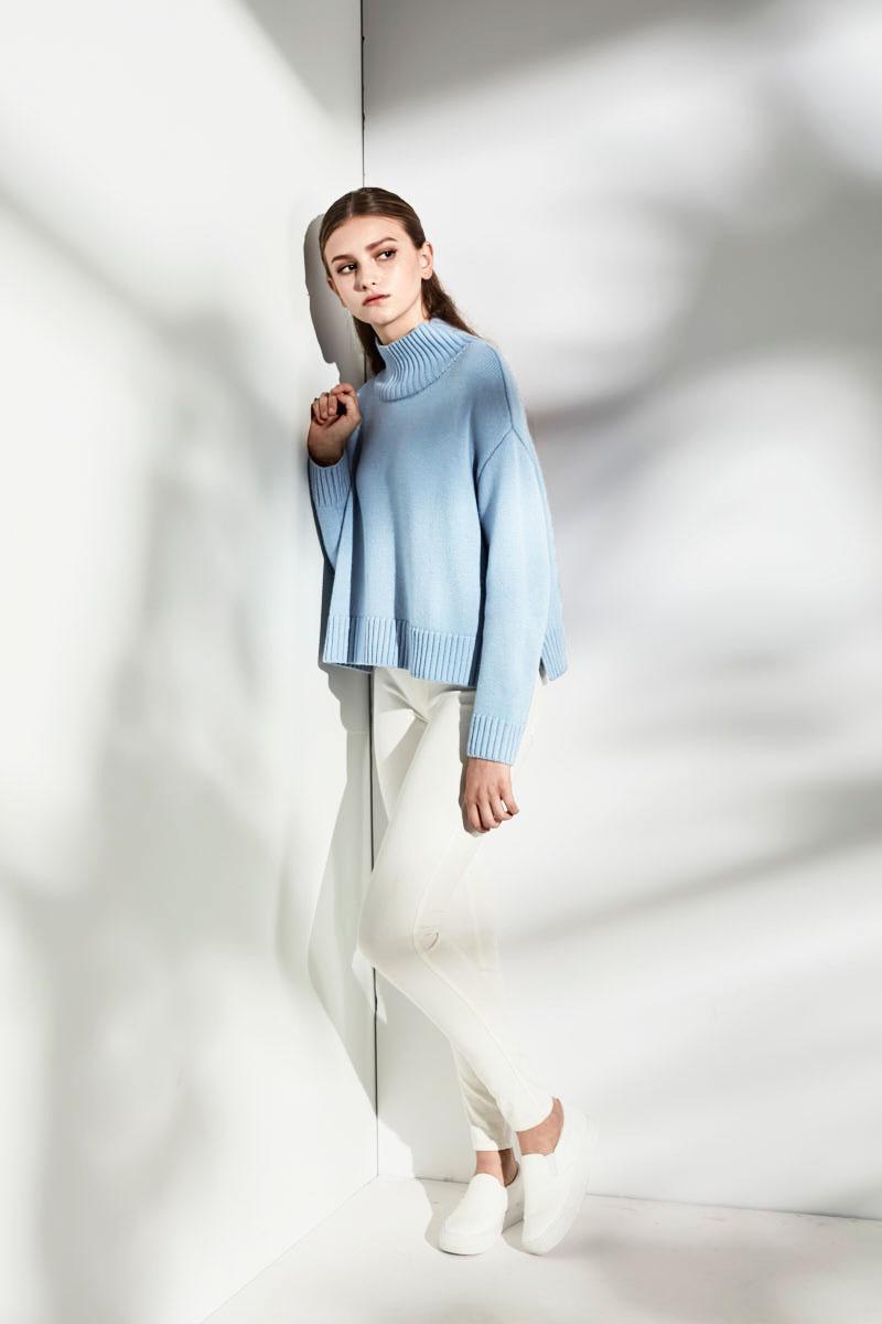 A model in an oversized light blue sweater and white trousers against a pale wall
