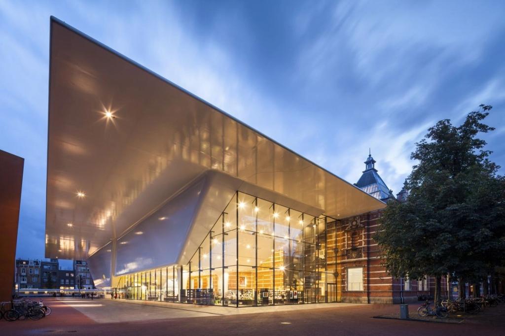 Белая нависающая пристройка музея Stedelijk и старое кирпичное здание в сумерках, Амстердам