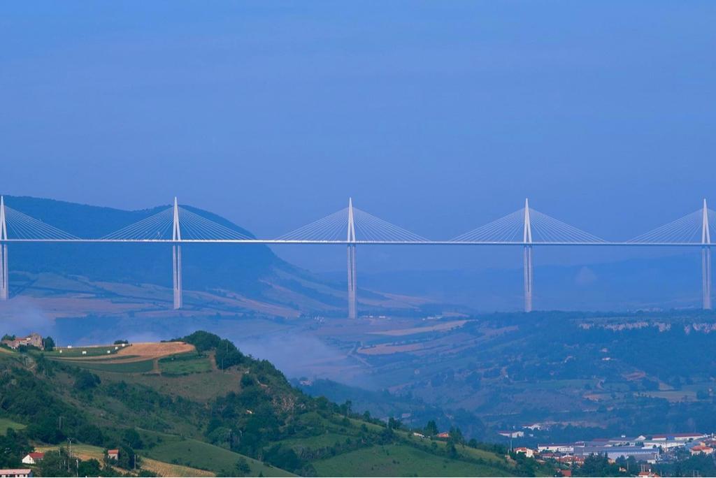 The cable-stayed Millau Viaduct stretching above a misty valley among green hills