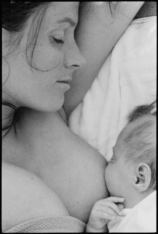 A young mother breastfeeds her sleeping newborn