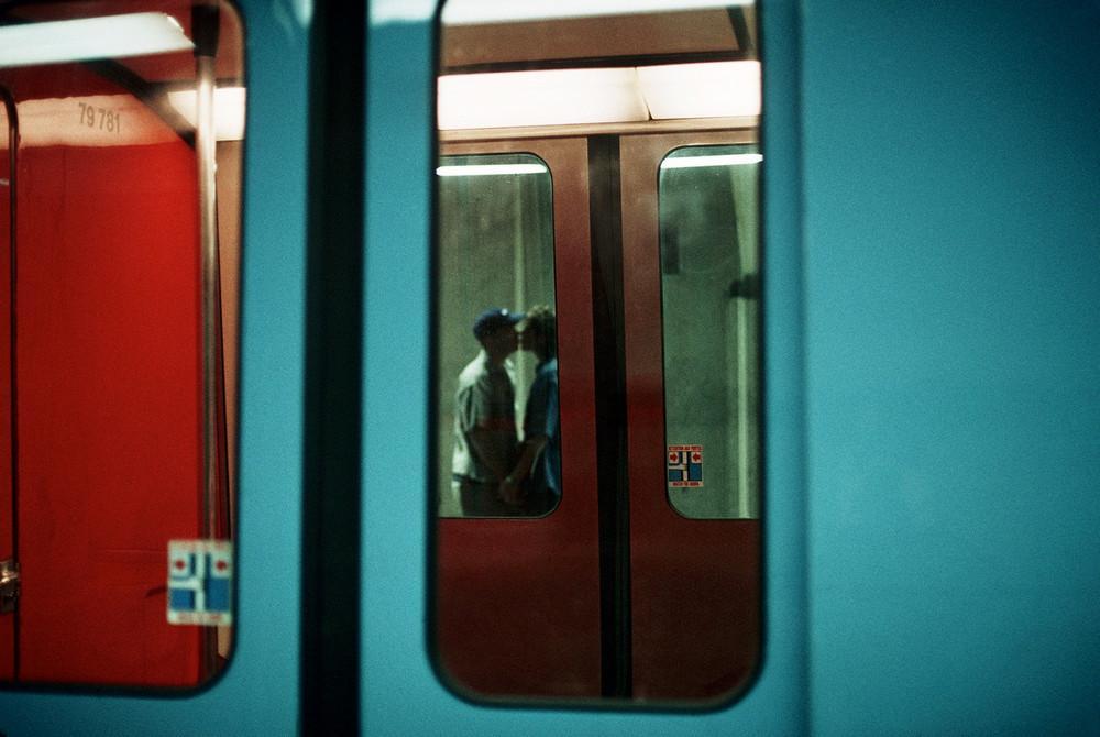 A kissing couple framed in the door window of a turquoise-and-red metro carriage