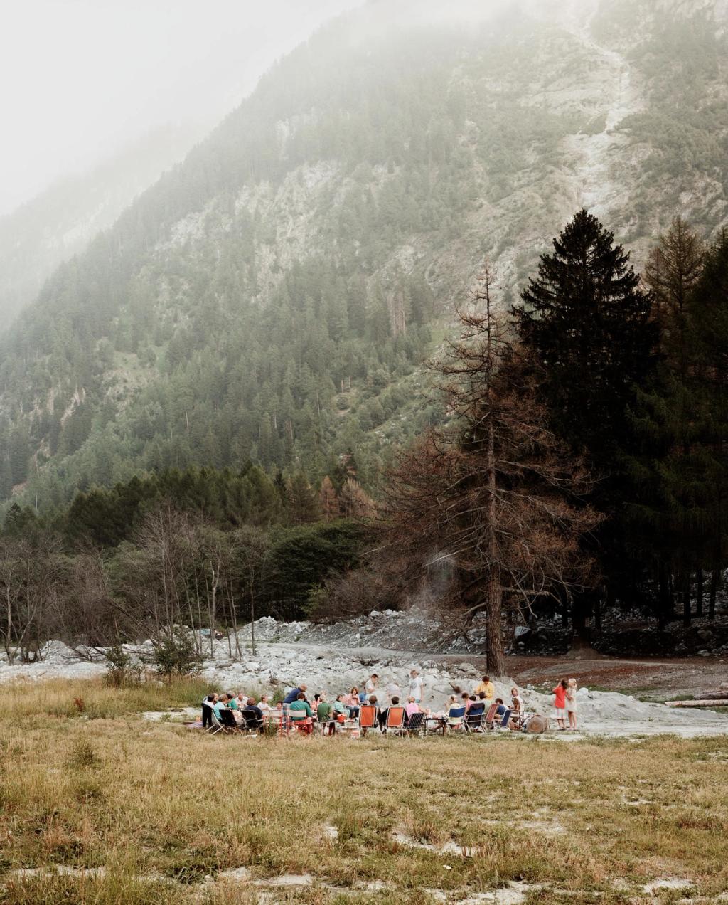 A group of people at a table on a meadow at the foot of a misty mountain slope with coniferous forest