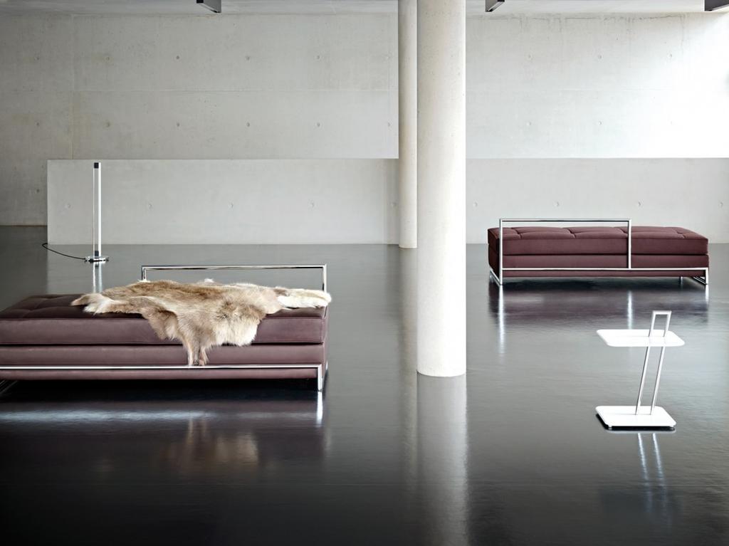 Eileen Gray's leather daybed with a hide throw, a second chaise longue and a side table in a concrete hall