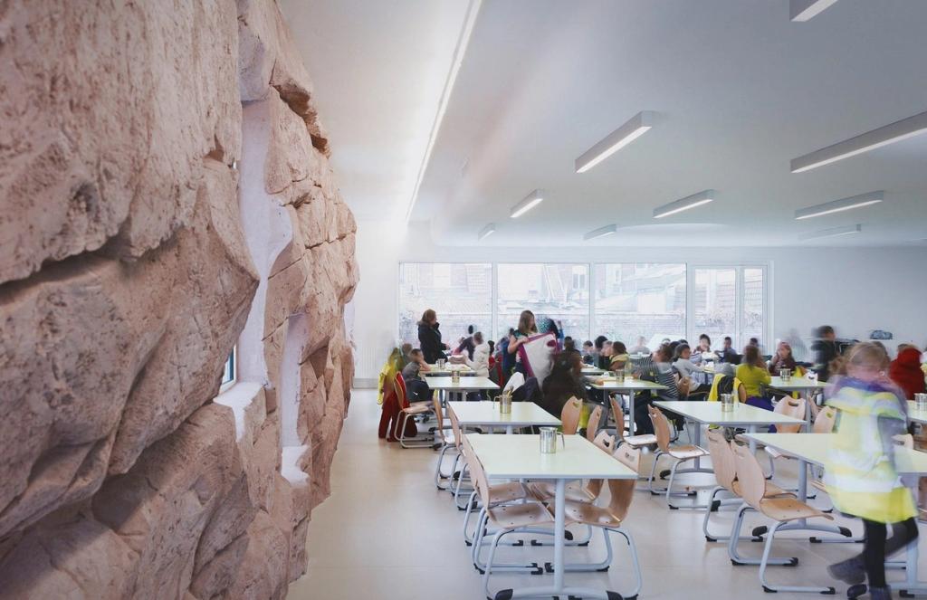 The bright canteen of The Roc School, with a textured wall in pink stone and children seated at tables