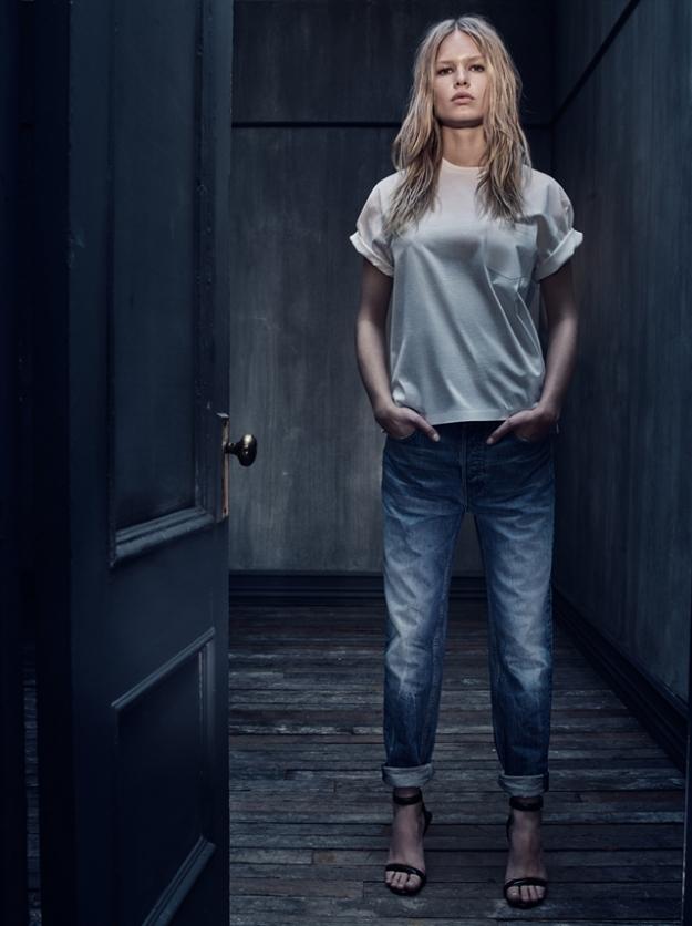 Model in a white silk T-shirt and worn jeans by a dark door