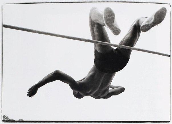 A high jumper in mid-flight over the bar, photographed from below against a pale sky