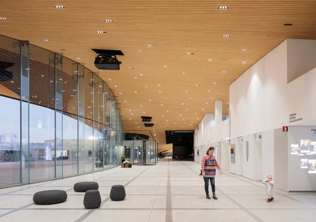 The spacious Oodi entrance hall with a slatted wooden ceiling, glass wall and grey upholstered poufs