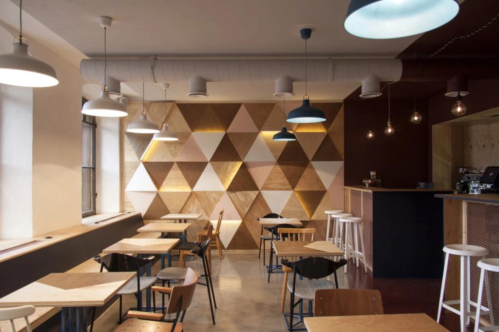 A café interior featuring an accent wall of wooden triangular panels and pendant lights