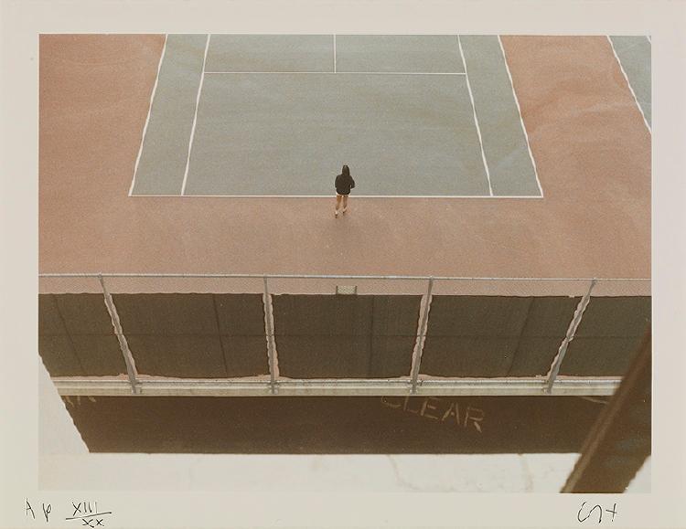 An aerial photograph of a tennis court with a solitary figure at its centre