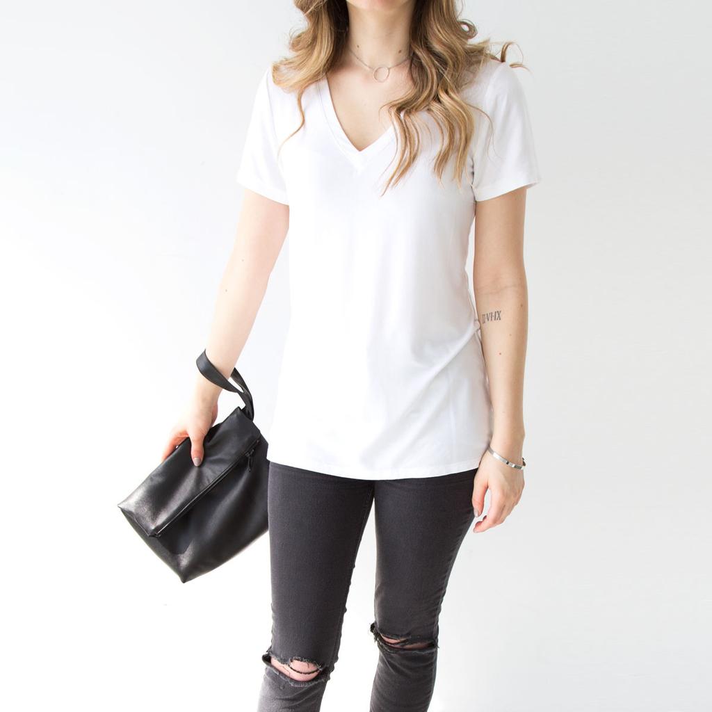 A woman in a white Encircled T-shirt and grey jeans, holding a black leather bag