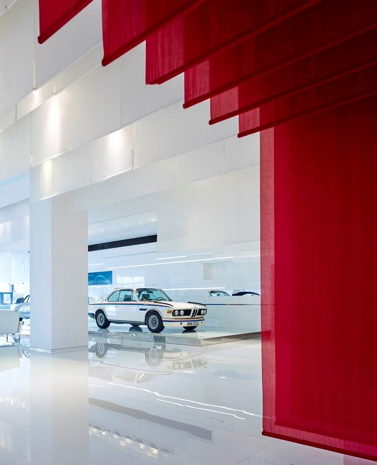 Белое классическое купе BMW, видимое сквозь свисающие красные текстильные полотна