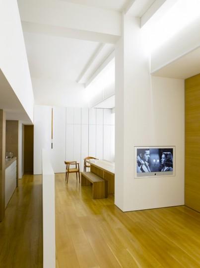 A bright interior with a wooden floor, a bench and a built-in television set into a white wall