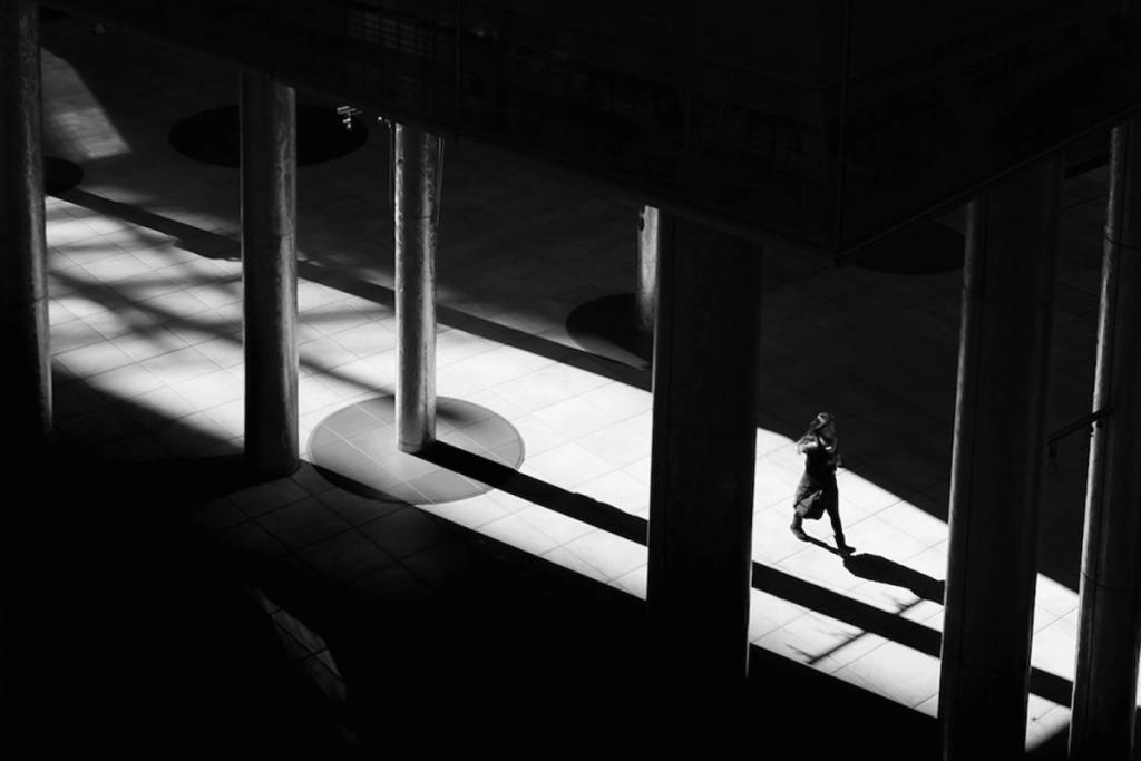 A person walks through a light-filled strip between columns, seen from above