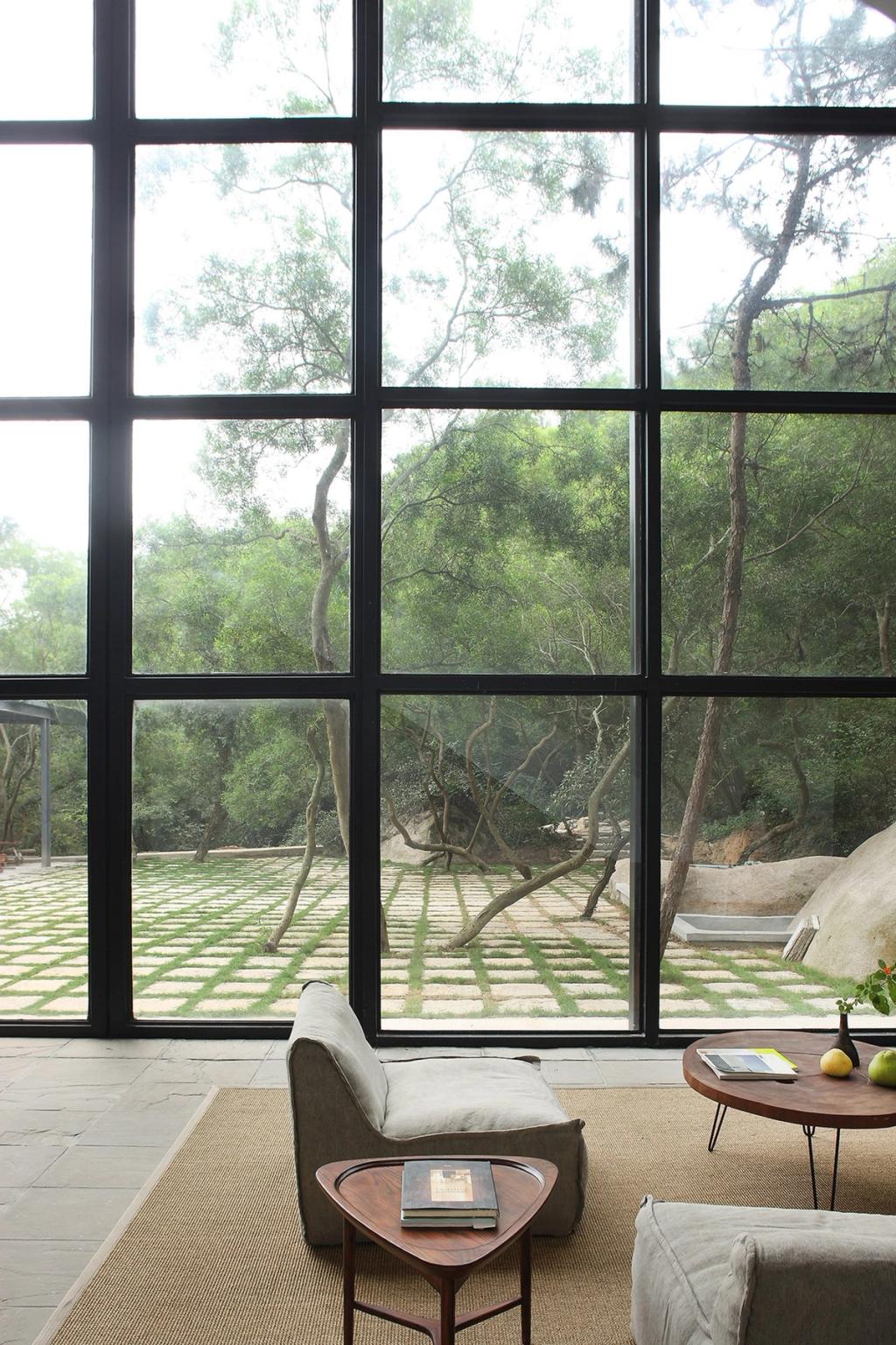 A bedroom and plunge pool behind a glass partition, with a boulder and a stone wall beside the forest