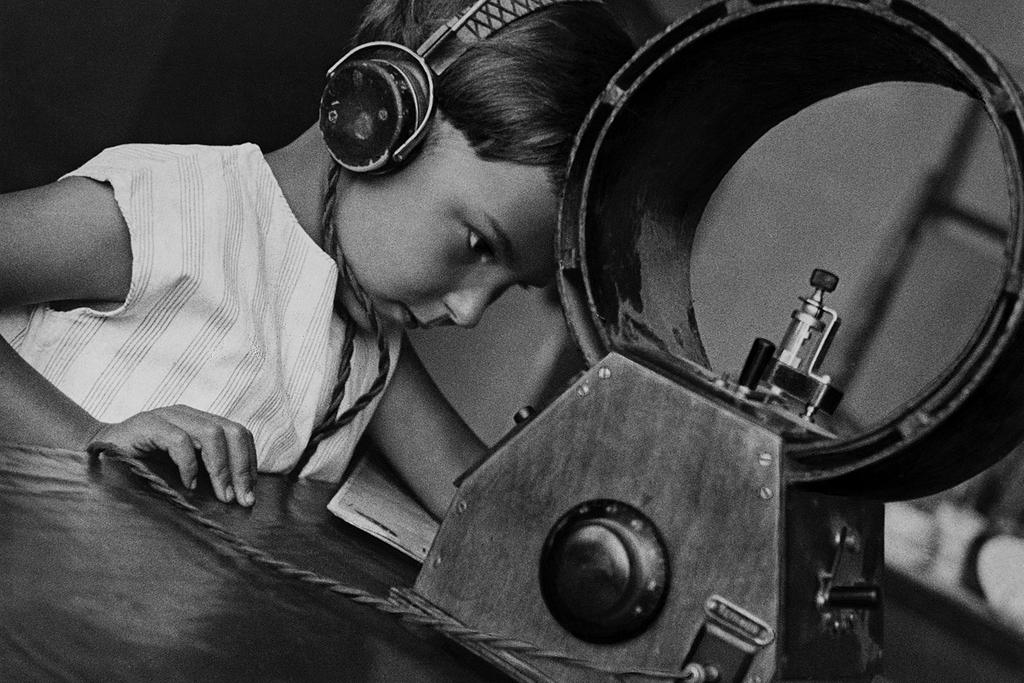 A boy in headphones bent over a radio receiver with a large horn
