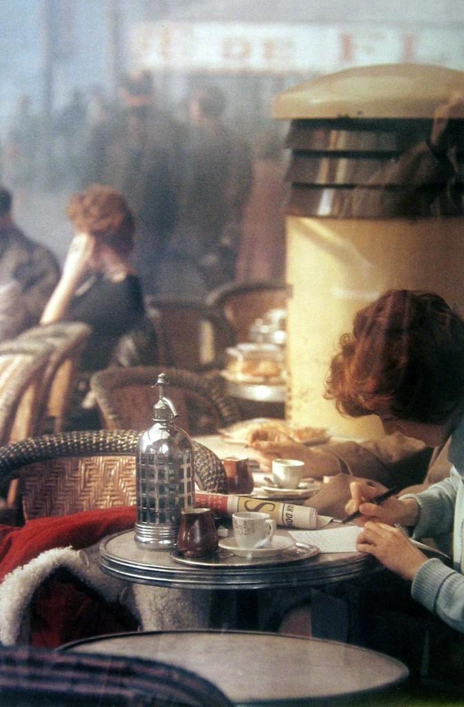 A café table with a siphon and a cup of coffee, customers visible through misted glass
