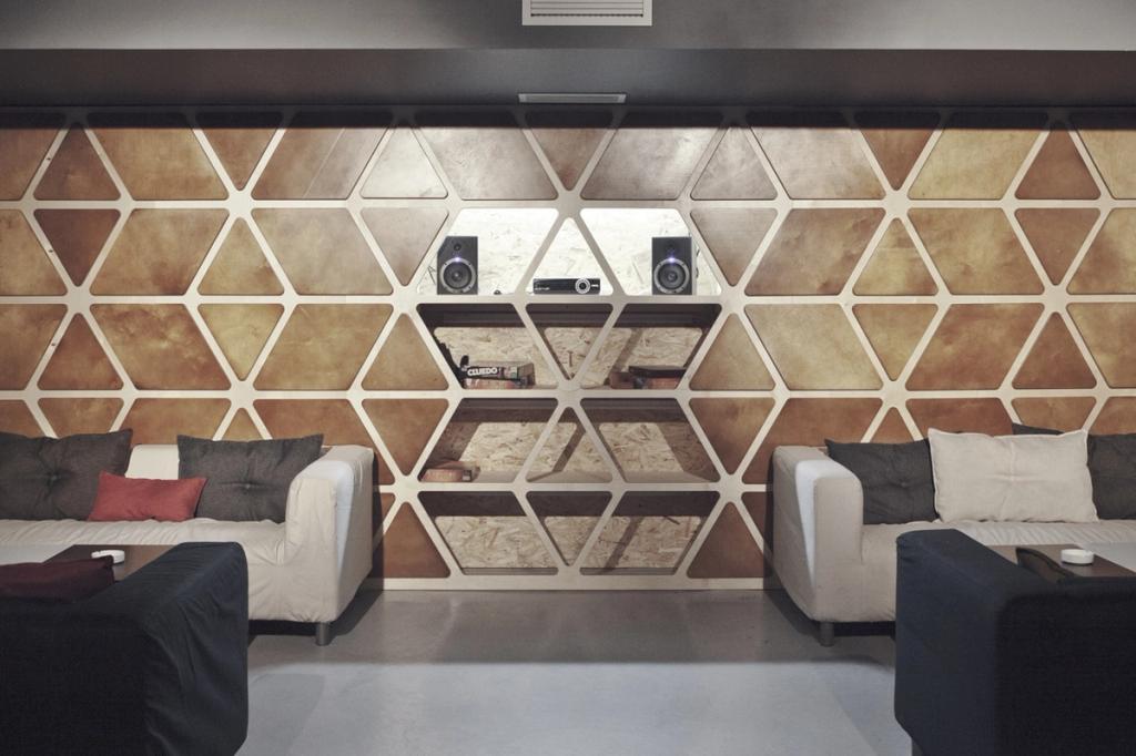 A lounge area with sofas and a wall of illuminated hexagonal wooden shelf modules
