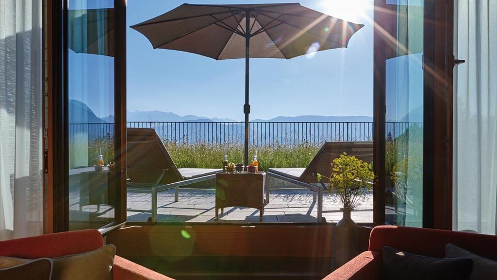 A room's terrace with sun loungers and a parasol, with a view of the Alpine peaks through the window