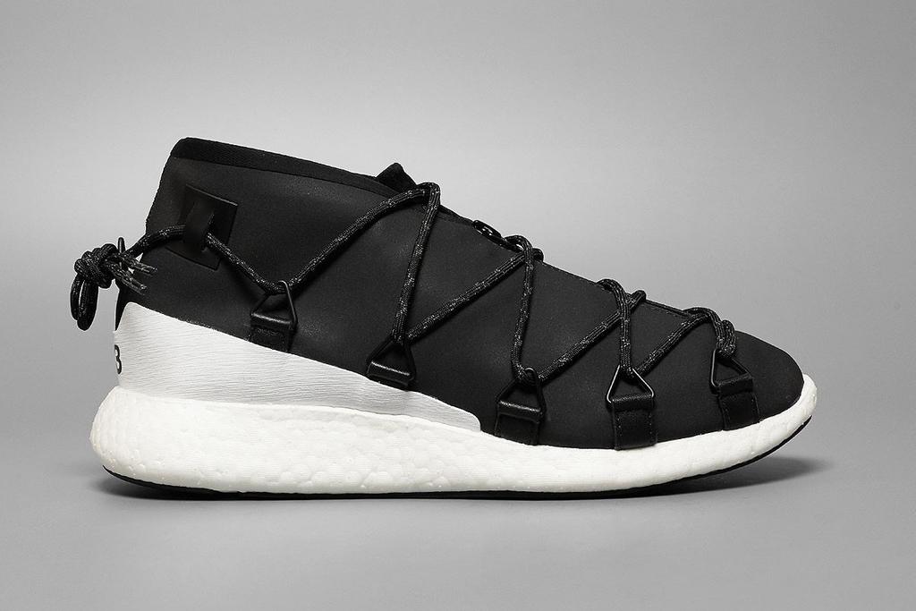 A black Y-3 tote bag held by a man in black clothing and trainers