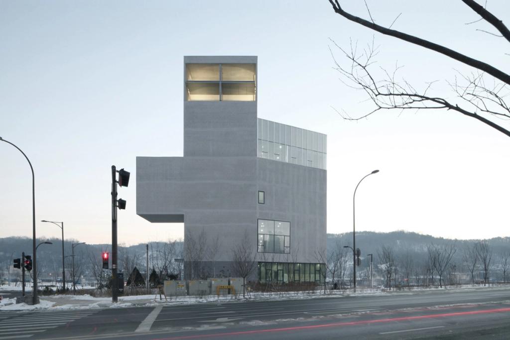 Уличный угол церкви RW Concrete Church в сумерках, верхний блок подсвечен изнутри