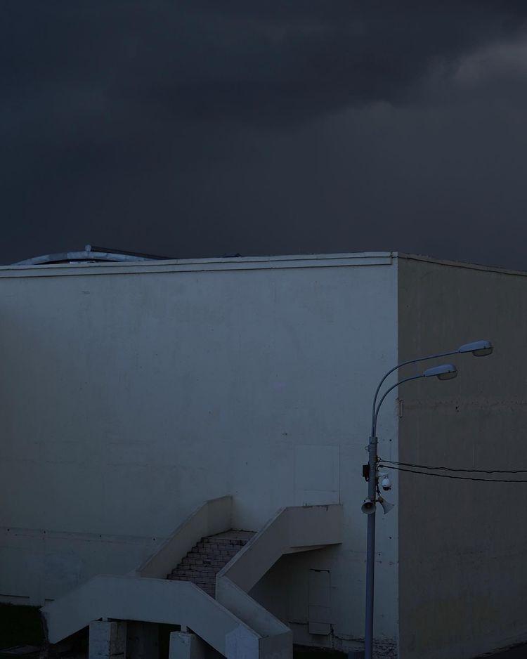 A pale concrete structure with a staircase and a street lamp beneath a dark, stormy sky