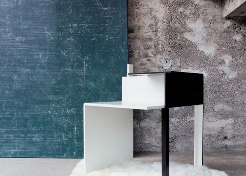 Eileen Gray's black-and-white bedside table against a concrete wall, with a sheepskin on the floor