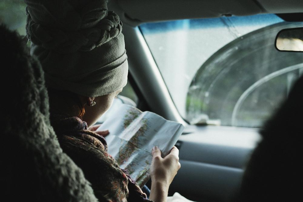 Девушка в платке изучает бумажную карту, сидя в салоне автомобиля