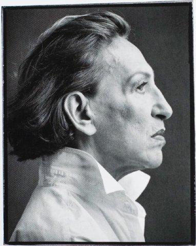 A profile portrait of a man with long hair swept back, set against a dark background