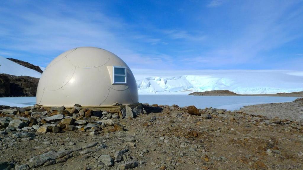 An individual dome cabin on a rocky shore beside a frozen lake