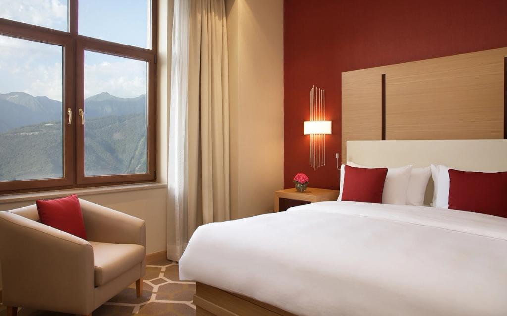 A Solis Sochi room with a red accent wall, a bed, and a window overlooking the mountains of Krasnaya Polyana